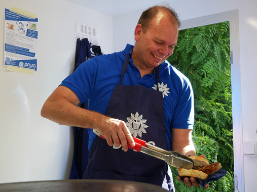 Foto zum Thema "Polizei Einsatzversorgung": Zu sehen ist Daniel Heyer am Grill. Er legt mit der Grillzange eine Wurst in ein Brötchen.