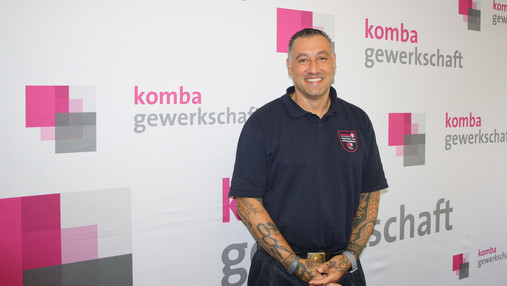 Foto zum Thema "Feuer im Wald": Zu sehen ist Valentino Tagliafierro. Er steht vor einer Leinwand mit dem Schriftzug und Logo der komba gewerkschaft.