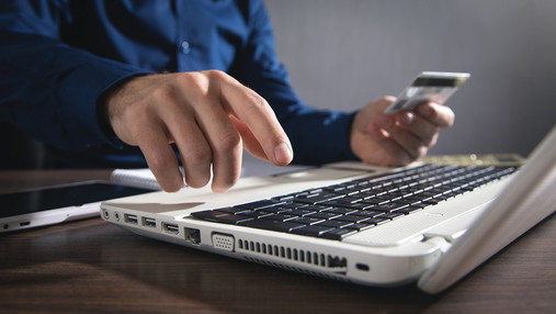 Zu sehen ist ein Mann, der am Laptop sitzt und seine Kreditkartendaten eintippt.