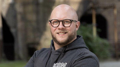 Foto zum Thema "Ausbildung zum Lebensmittelkontrolleur": Zu sehen ist Florian, der als Lebensmittelkontrolleur in Mönchengladbach arbeitet. Er trägt einen schwarzen Hoodie, seine Arme sind verschränkt.