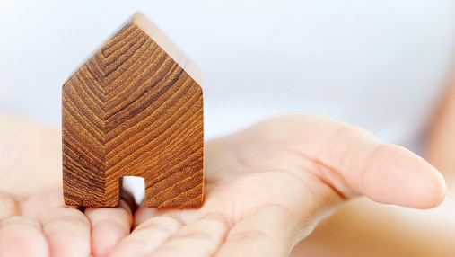 Zu sehen sind Hände, die Handflächen nach oben gewendet. Darauf steht ein Modellhäuschen.