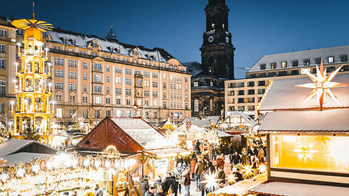 Foto zum Thema "Dresdner Striezelmarkt": Zu sehen ist der Markt, die Lichter leuchten in der Dunkelheit. Links im Bild ist die Weihnachtspyramide.