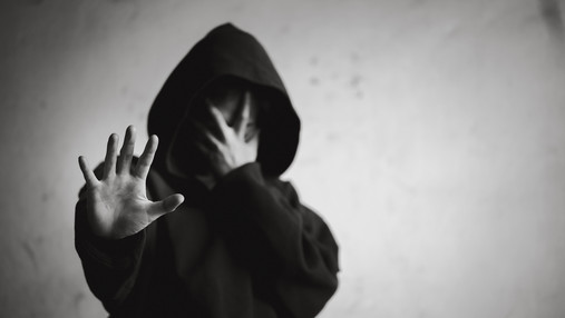 Foto zum Thema Sucht-Kriterien: Zu sehen ist eine verzweifelte Person mit einem Hoodie, die die Hand abweisend nach vorne streckt.