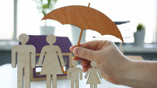 Foto zum Thema "wichtige Versicherungen": Zu sehen sind Figuren, die eine Familie darstellen, darüber ein schützender Regenschirm.