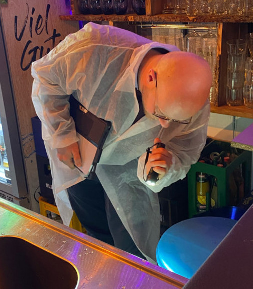 Foto zum Thema "Ausbildung zum Lebensmittelkontrolleur": Zu sehen ist Lebensmittelkontrolleur Florian Ackens, der in einer Bar mit einer Taschenlampe unter die Spüle leuchtet.