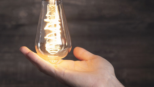 Foto zum Thema "Dynamische Stromtarife": Zu sehen ist eine leuchtende Glühbirne, darunter eine Hand, die die Glühbirne berührt.