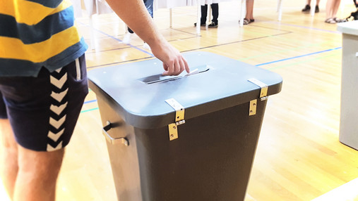 Foto zum Thema "Verwaltung für Demokratie": Zu sehen ist eine Wahlurne, außerdem der Arm einer Person, die gerade ihre Stimme abgibt.