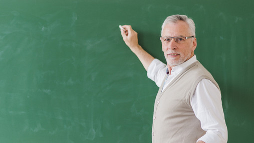 Foto zum Thema Remonstrationspflicht: Zu sehen ist ein Lehrer, der ein Stück Kreide in der Hand hält und an der Tafel steht.