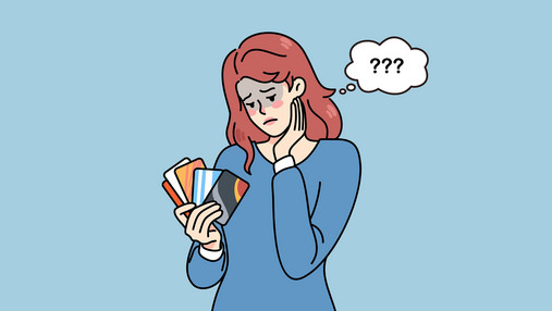 Zu sehen ist eine Frau, die ratlos auf ihre Kreditkarten schaut, die sie wie ein Fächer in der Hand hält.