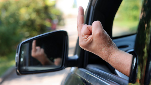 Foto zum Thema "im Dienst beleidigt": Zu sehen ist jemand, der aus einem geöffneten Autofenster den Stinkefinger zeigt.