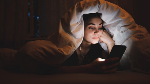 Foto zum Thema Mediensucht bei Jugendlichen: Eine junge Frau liest im Bett Nachtrichten auf dem Smartphone. 
