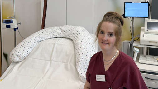 Foto zum Thema "Wie wird man Hebamme": Zu sehen ist Annina auf Station. Sie sitzt neben einem Bett.