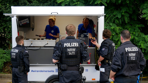Foto zum Thema "Polizei Einsatzversorgung": Zu ist eine Gruppe Polizisten, die sich vor dem Versorgungswagen versammelt hat.