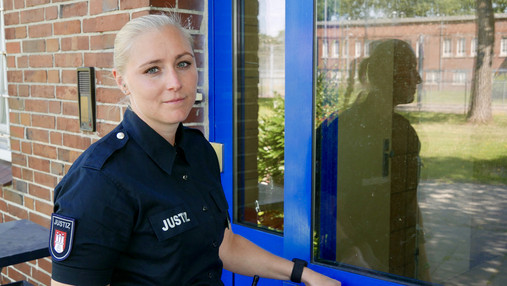 Foto zum Thema "JVA Hahnöfersand": Zu sehen ist Justizvollzugsbeamtin Dammann. Sie steht vor einer Tür und schaut in die Kamera.