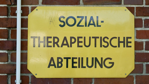 Foto zum Thema "JVA Hahnöfersand": Zu sehen ist ein Schild mit der Aufschrift "Sozialtherapeutische Abteilung", das an einer roten Backsteinmauer befestigt ist.