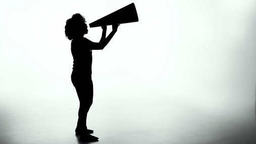 Foto zum Thema "Kürzungen Soziale Arbeit": Zu sehen sind die schattigen Umrisse einer Person mit einem Megafon in der Hand.