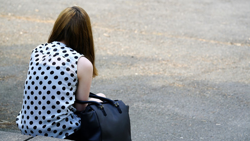 Foto zum Thema "Kinder- und Jugendtelefon": Zu sehen ist ein Mädchen, das geknickt auf einem Kantstein sitzt und den Rücken zugewandt hat.