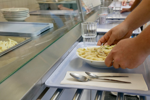 Foto zum Thema "JVA Hahnöfersand": Zu sehen ist eine Nahaufnahme bei der Essensausgabe. Abgebildet ist ein Tablet mit Pasta und Besteck, die Hände eines Gefangenen sind ebenfalls zu sehen.